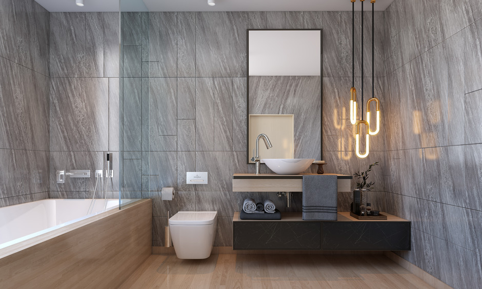 Bathroom interior design featuring grey marble walls, ceramic bathtub, and wooden flooring.